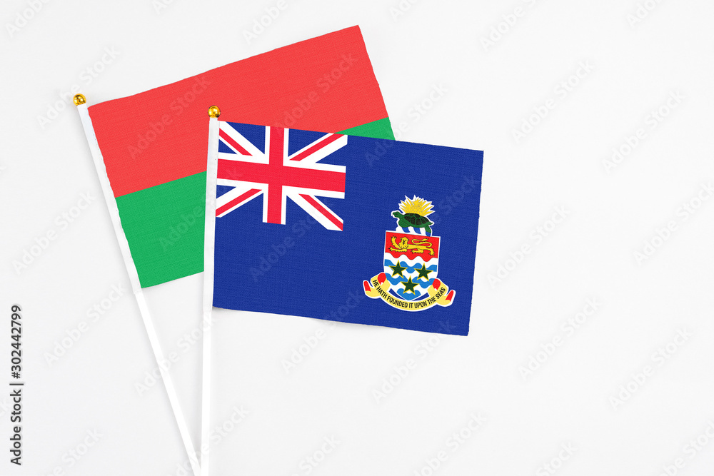 Fototapeta premium Cayman Islands and Burkina Faso stick flags on white background. High quality fabric, miniature national flag. Peaceful global concept.White floor for copy space.