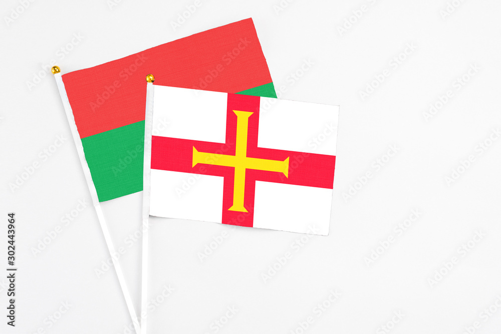 Guernsey and Burkina Faso stick flags on white background. High quality fabric, miniature national flag. Peaceful global concept.White floor for copy space.