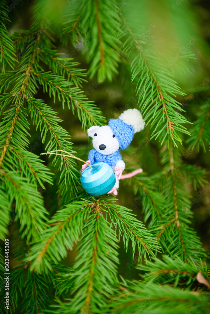Obraz premium Knitted white mouse with a blue christmas ball on the christmas tree. Symbol of the New Year 2020.