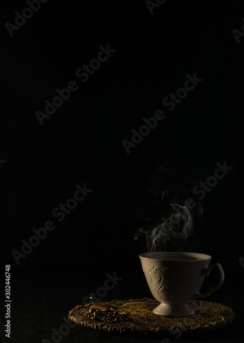 A cup of hot coffee accompanied by coffee beans on a black background.
