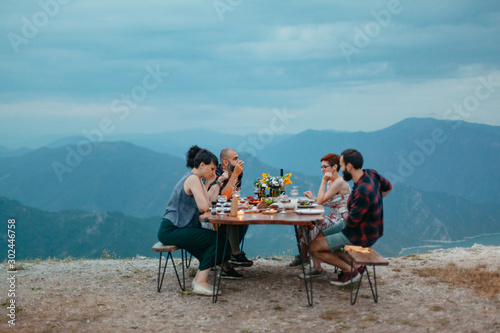 Friends and family gathered for picnic dinner for Thanksgiving. Festive young people celebrating life with red wine, grapes, cheese platter, and a selection of cold meats © Suteren Studio