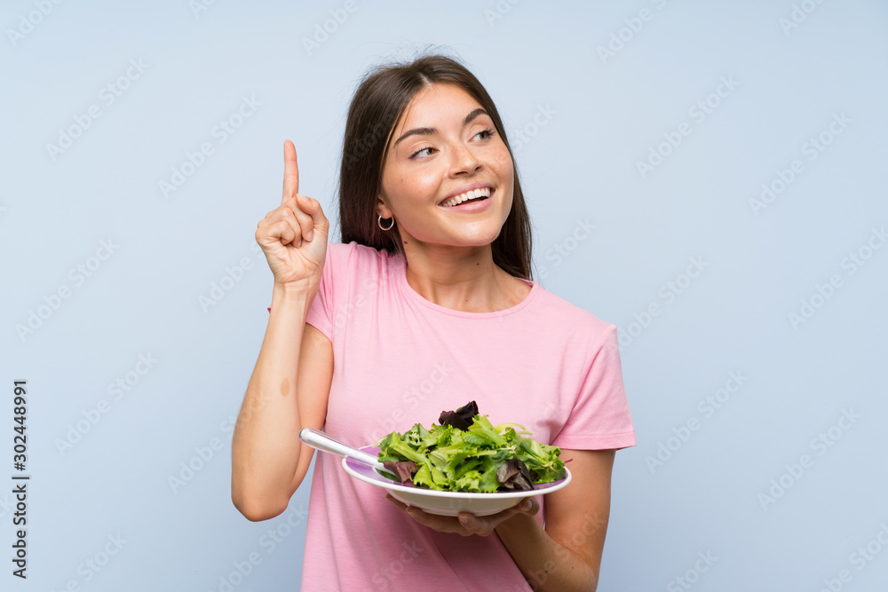 Young woman with salad over isolated blue background intending to realizes the solution while lifting a finger up Young woman with salad over isolated blue background intending to realizes the solution while lifting a finger up