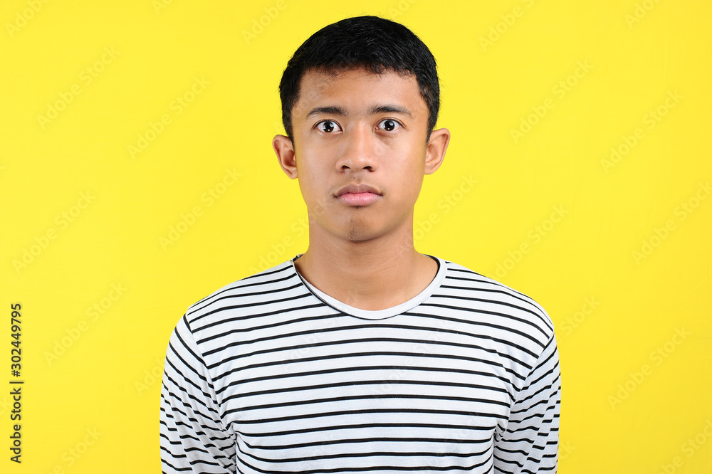 Very serious young Asian man looking at camera isolated on yellow Very serious young Asian man looking at camera isolated on yellow
