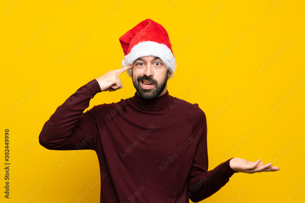 Man with christmas hat over isolated yellow background making the gesture of madness putting finger on the head Man with christmas hat over isolated yellow background making the gesture of madness putting finger on the head
