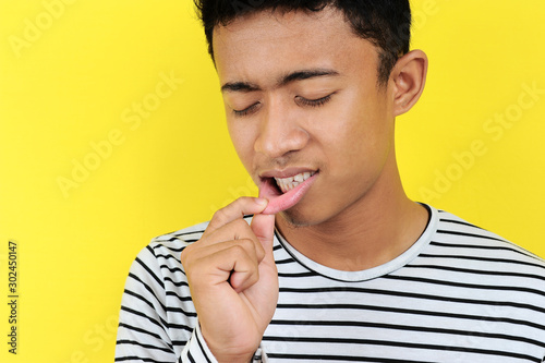Young Asian man showing ulcer or blister in his mouth at camera, isolated on yellow photo