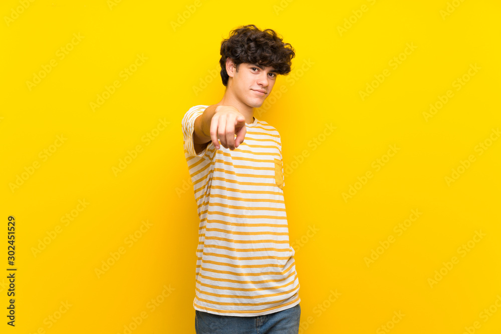 Young man over isolated yellow wall points finger at you with a confident expression