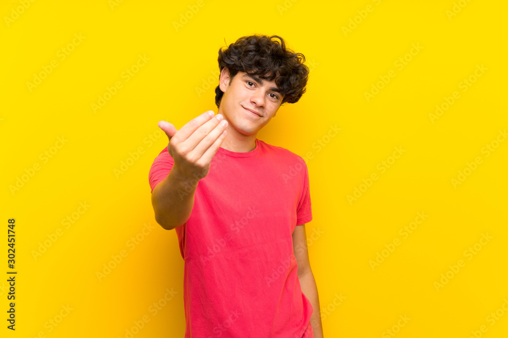 Young man over isolated yellow wall inviting to come Young man over isolated yellow wall inviting to come