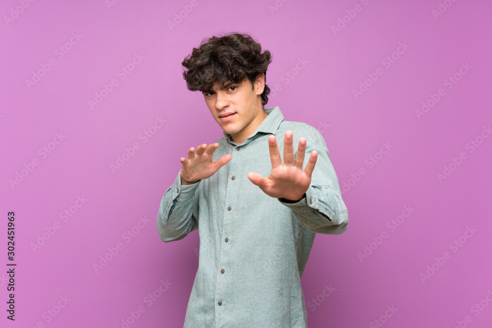 Young man over isolated purple wall nervous stretching hands to the front