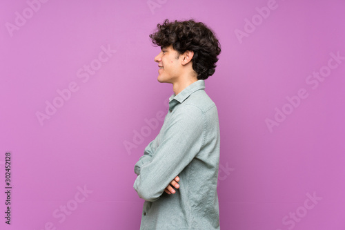 Young man over isolated purple wall in lateral position