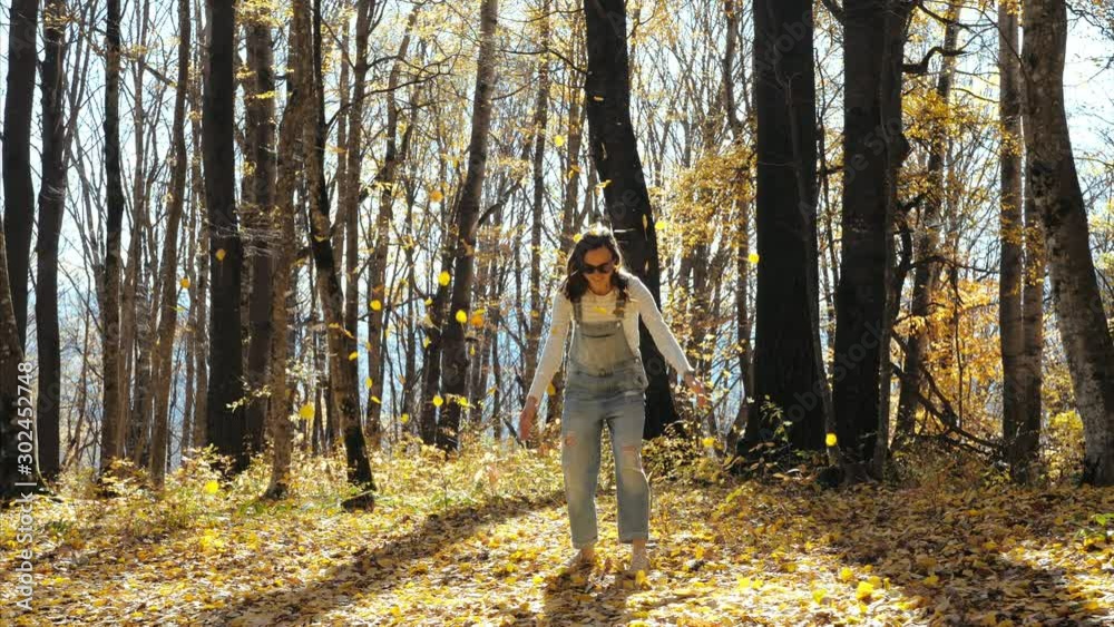 Happy young woman having fun, laughing and throwing yellow leaves at autumn forest in sunny day. Leaves is falling with backlit. Fall season concept. Happy young woman having fun, laughing and throwing yellow leaves at autumn forest in sunny day. Leaves is falling with backlit. Fall season concept.
