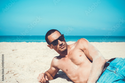 young muscular man resting and posing on the beach. 