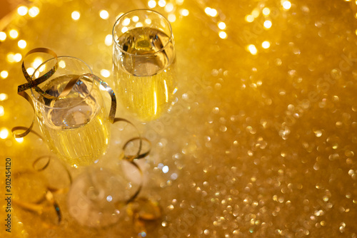 Top view two glasses of champagne on golden glittering background with defocused lights. Christmas and New Year holidays concept. Copy space. Soft focus