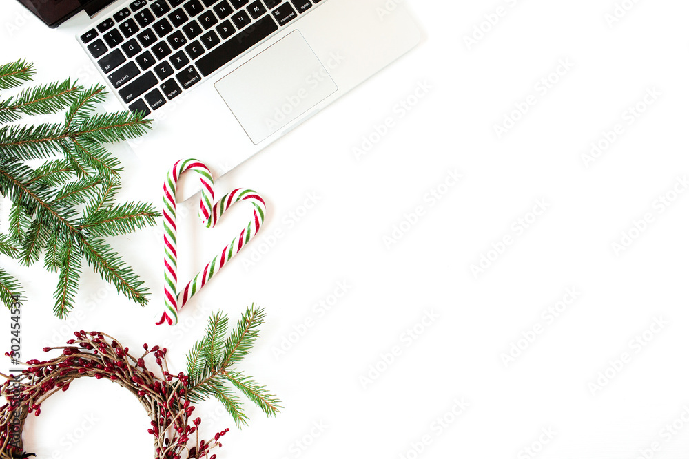 Christmas / New Year holiday composition. Home office desk with laptop, Christmas baubles / balls, fir branches, candy sticks on white background. Flat lay, top view festive business concept. - obrazy, fototapety, plakaty 