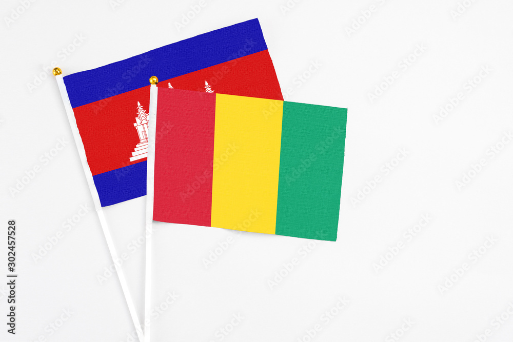 Fototapeta premium Guinea and Cambodia stick flags on white background. High quality fabric, miniature national flag. Peaceful global concept.White floor for copy space.