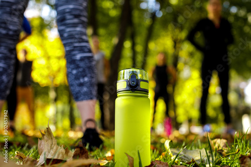 bottle of water on green grass. sporty women doing outdoor workout in park on background. focus on bottle