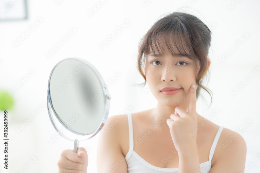 Beautiful young asian woman looking the mirror with acne problem at bedroom, trouble of beauty on face, zit treatment, asia girl is pimple having worry and displeased, skincare and healthy concept. Beautiful young asian woman looking the mirror with acne problem at bedroom, trouble of beauty on face, zit treatment, asia girl is pimple having worry and displeased, skincare and healthy concept.