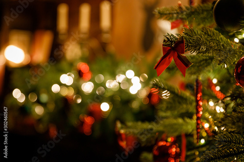 Christmas and New Year interior - blur background: fireplace, lamps, green Christmas tree, brown leather sofa, gifts, candles, moose rocking chair. Lots of lights glowing in the dark.