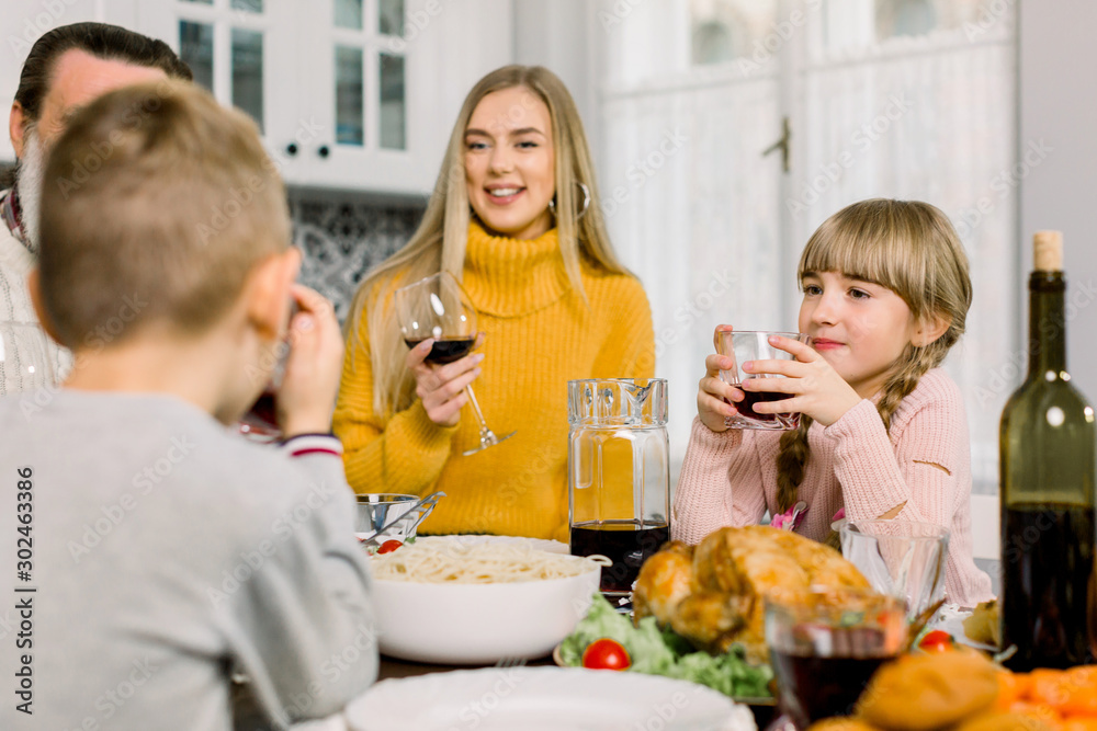 happy young mother and cute little daughter holding glasses with drinks at thanksgiving holiday table. Family dinner, mother with children boy and girl, grandfather at the table
