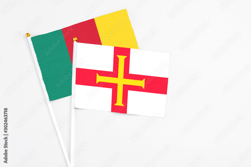 Guernsey and Cameroon stick flags on white background. High quality fabric, miniature national flag. Peaceful global concept.White floor for copy space.