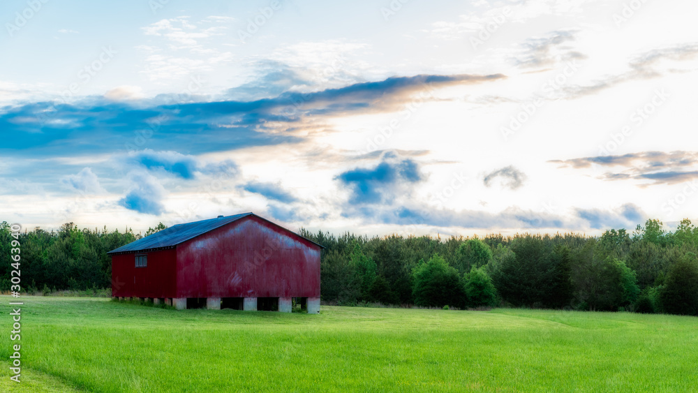 Red barn in a field with sky and clouds in the background Red barn in a field with sky and clouds in the background