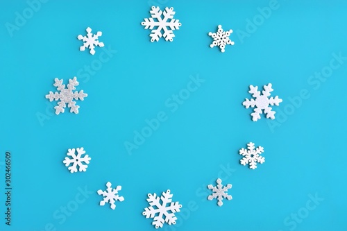 Blue Christmas background with shiny silver and white snowflakes border and empty space for text, selective focus. New year flat lay with snowflakes decorative border. Winter postcard