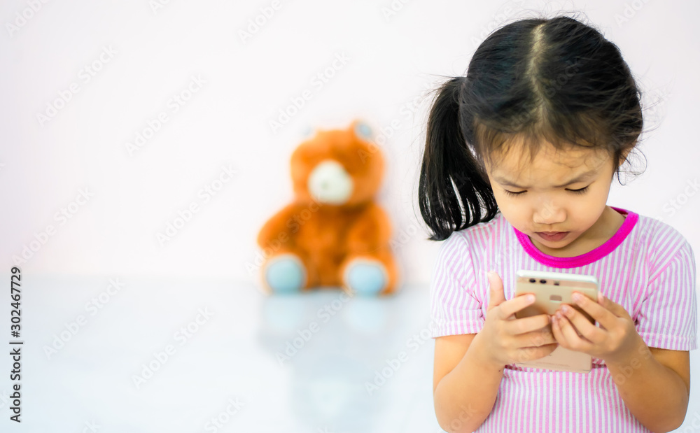 an Asian girlThe kindergartener was playing the phone with fun, ignoring the doll beside her an Asian girlThe kindergartener was playing the phone with fun, ignoring the doll beside her