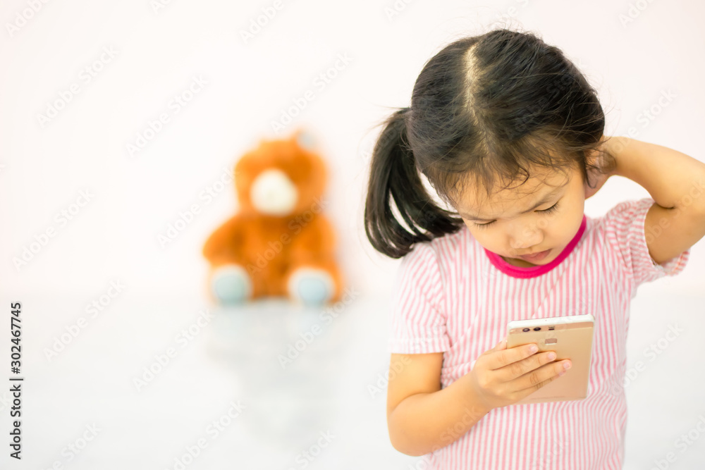 an Asian girlThe kindergartener was playing the phone with fun, ignoring the doll beside her an Asian girlThe kindergartener was playing the phone with fun, ignoring the doll beside her