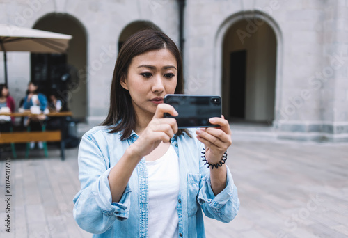 Attractive tourist taking pictures and shooting video on mobile phone for publication in internet networks via 4G internet standing in historic center with public wifi, Asian woman clicking images photo