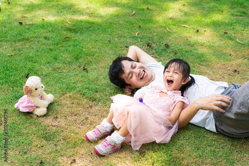 Asian father and daughter are lay down and laughing together with fully happiness moment while the are playing the soap bubbles in the green park, concept of activity for family lifestyle.