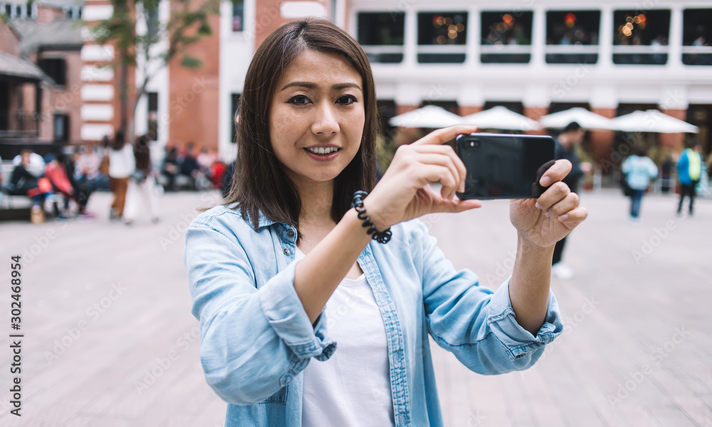 Portrait of happy woman photographing urban view with mobile phone camera during travel journey, Japanese millennial female tourist taking picture with smartphone enjoying trip time for recreating
