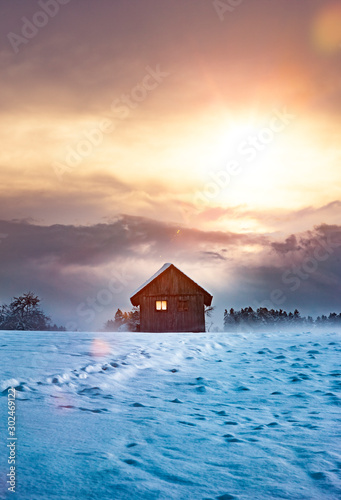 Blockhaus mit Leuchtendem Fenster im Winter bei Dämmerung