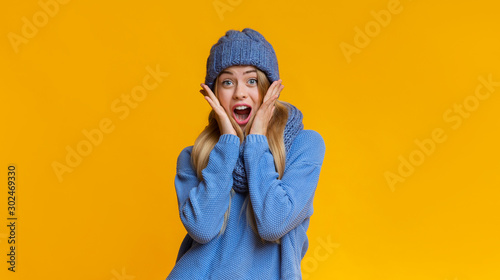 Amazed girl in winter hat touching her cheeks with palms