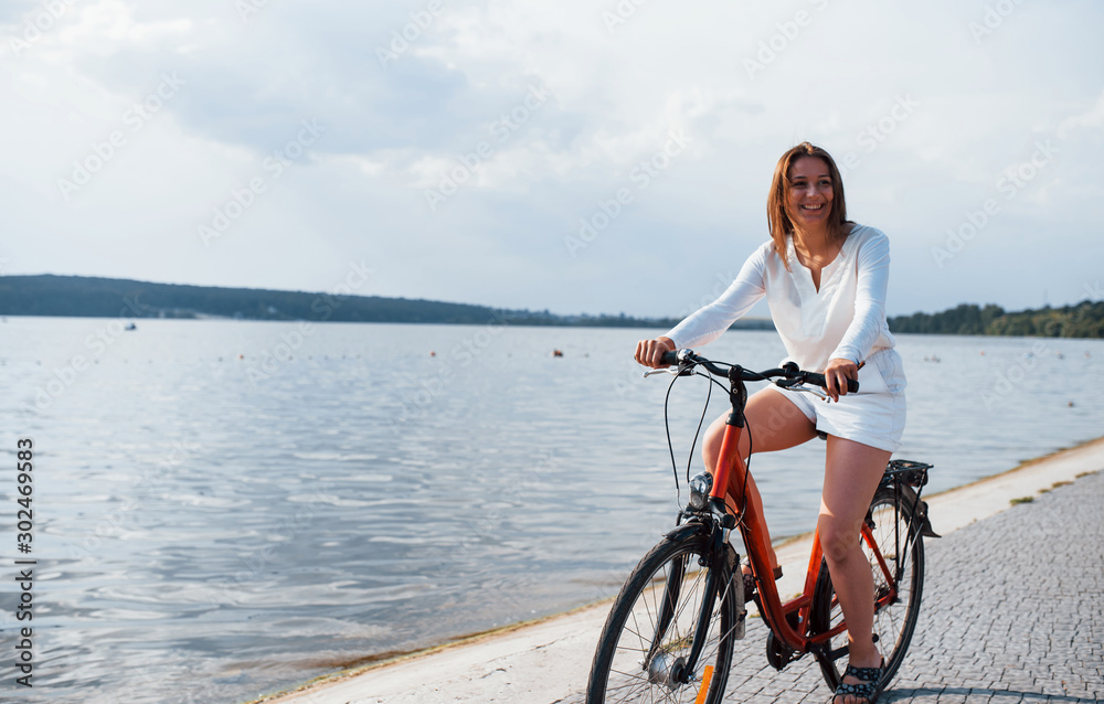 Fototapeta premium Cheerful girl rides bike on the beach near the lake at sunny daytime