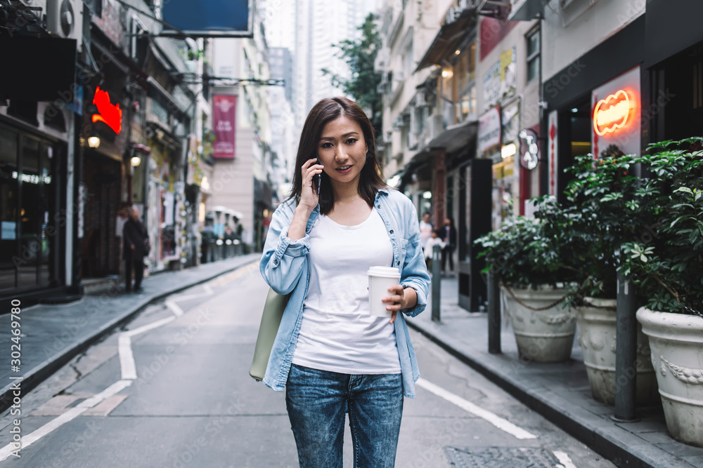 Smiling Asian woman talking on cellphone on street with coffee