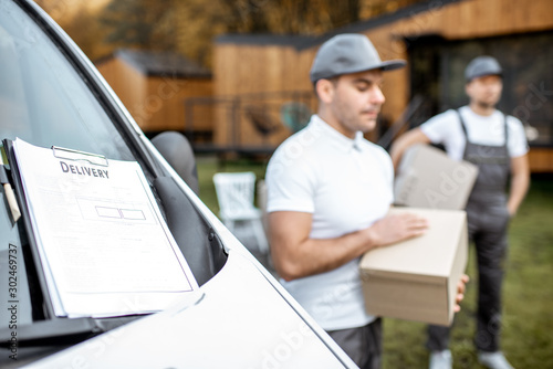 Delivery checklist on the vehicle's windshield and couriers with parcels on the background