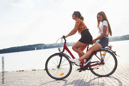 Two female friends on the bike have fun at beach near the lake © standret