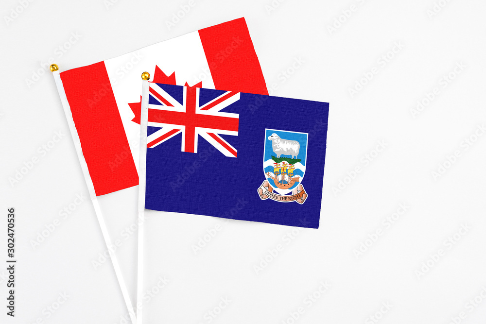 Fototapeta premium Falkland Islands and Canada stick flags on white background. High quality fabric, miniature national flag. Peaceful global concept.White floor for copy space.