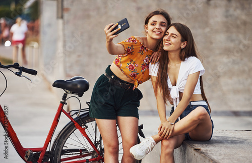 Making a selfie. Two young women with bike have a good time in the park