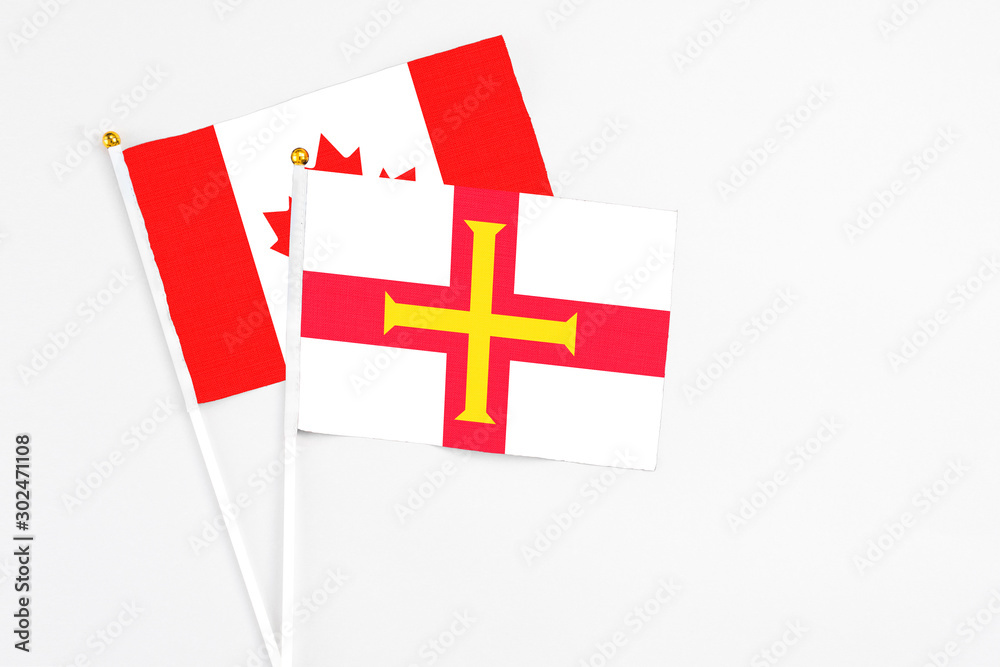 Guernsey and Canada stick flags on white background. High quality fabric, miniature national flag. Peaceful global concept.White floor for copy space.