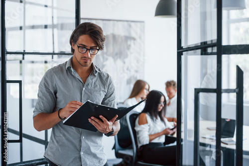 Man in glasses with notepad and pen in hands stands in the office opposite employees