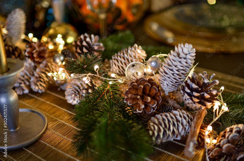 Christmas decorations on a large wooden table. Fir cones and branches are sprinkled with snow and decorated with a garland.
