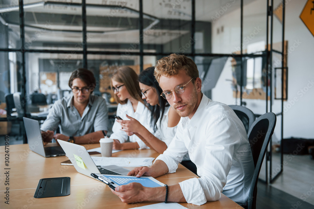 © standret - Blonde guy in glasses is in front of employees. Young business people in formal clothes working in the office © standret - Blonde guy in glasses is in front of employees. Young business people in formal clothes working in the office