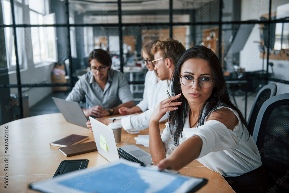 Brunette woman in front of employees. Young business people in formal clothes working in the office Brunette woman in front of employees. Young business people in formal clothes working in the office