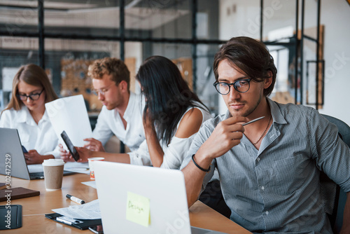 Guy in glasses in front of his employees. Young business people in formal clothes working in the office photo