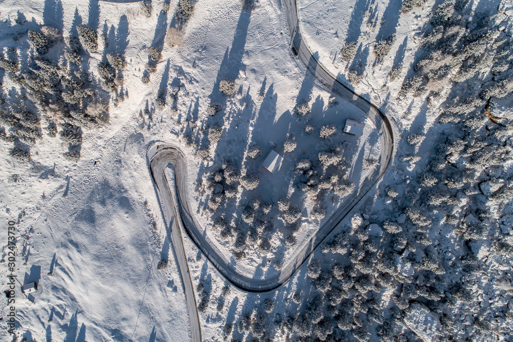 Curved road in the Italian Alps in South Tyrol, during winter / Sunny winter day with harsh shadows and lot of snow