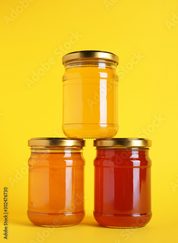 Jars with different types of organic honey on yellow background photo