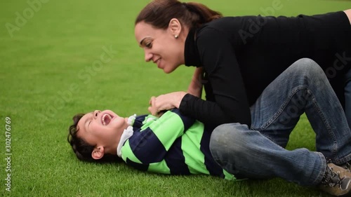 Loving mother and child playing in the grass, having fun and tickling