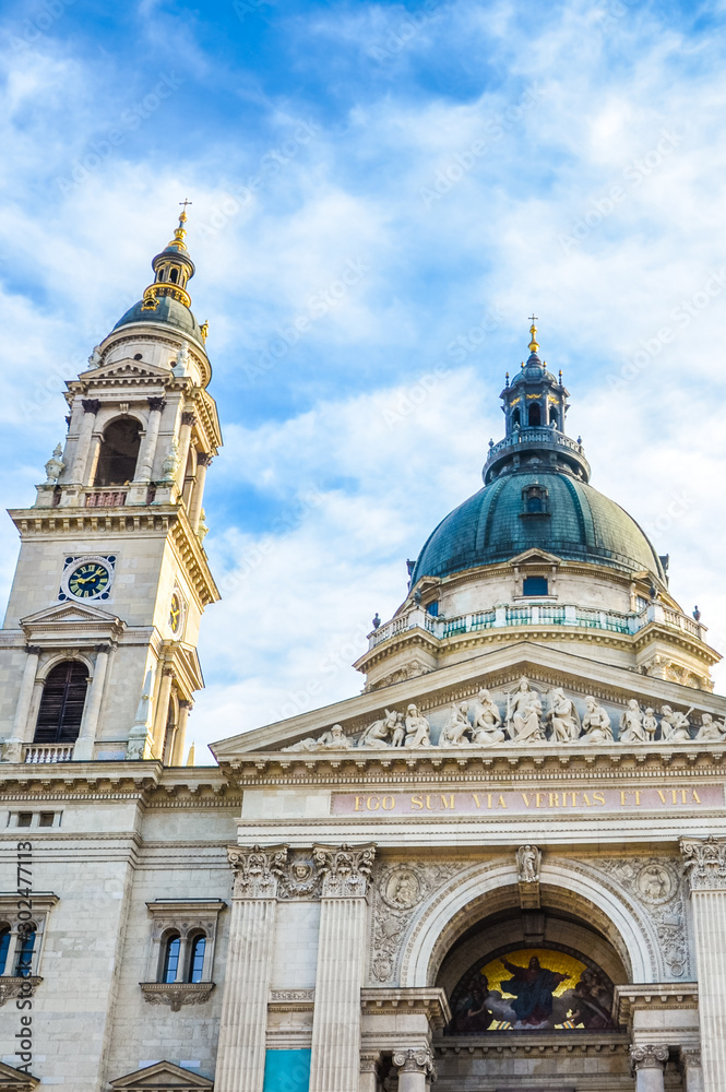 Vertical picture of the front side facade of Saint Stephen's Basilica in Budapest, Hungary with blue sky and clouds above. Roman Catholic basilica built in neoclassical style. Left tower and cupola