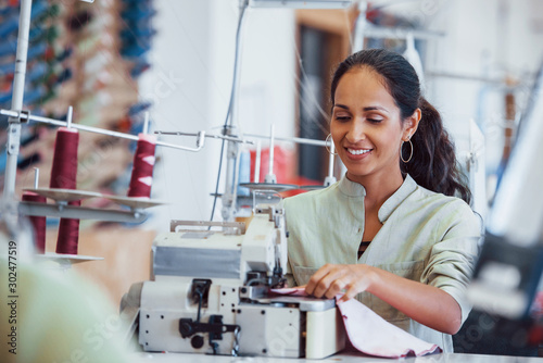 Dressmaker woman sews clothes on sewing machine in factory