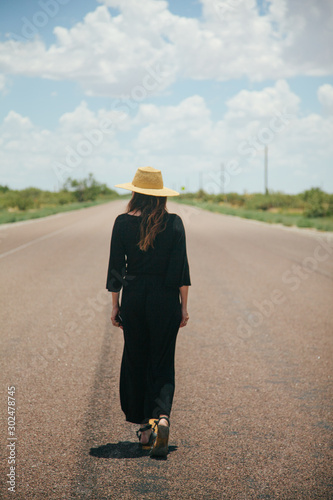 Woman in Hat With Back to Camera Stands in Middle of Empty Texas Highway Looking Out